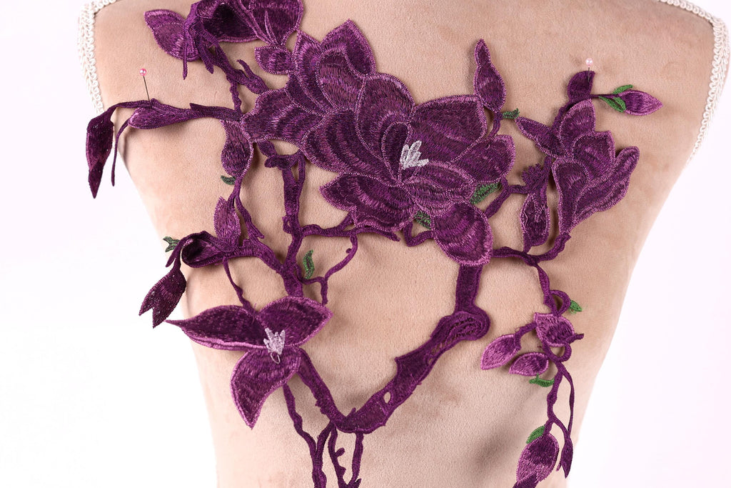 a mannequin with a back adorned with a large, intricate purple floral embroidery. The embroidery is composed of numerous purple flowers and leaves, creating a visually striking and detailed design. The mannequin is positioned in a way that highlights the craftsmanship and artistry of the embroidery.