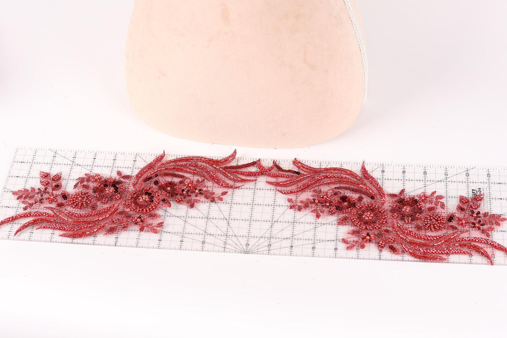 a decorative red lace piece with intricate floral patterns, placed on a ruler for scale.