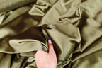 A hand is holding a piece of green satin fabric, examining it closely.