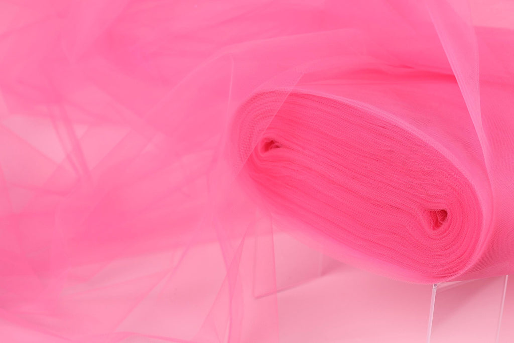 A close-up view of a pink fabric, possibly tulle, with a soft, flowing texture.