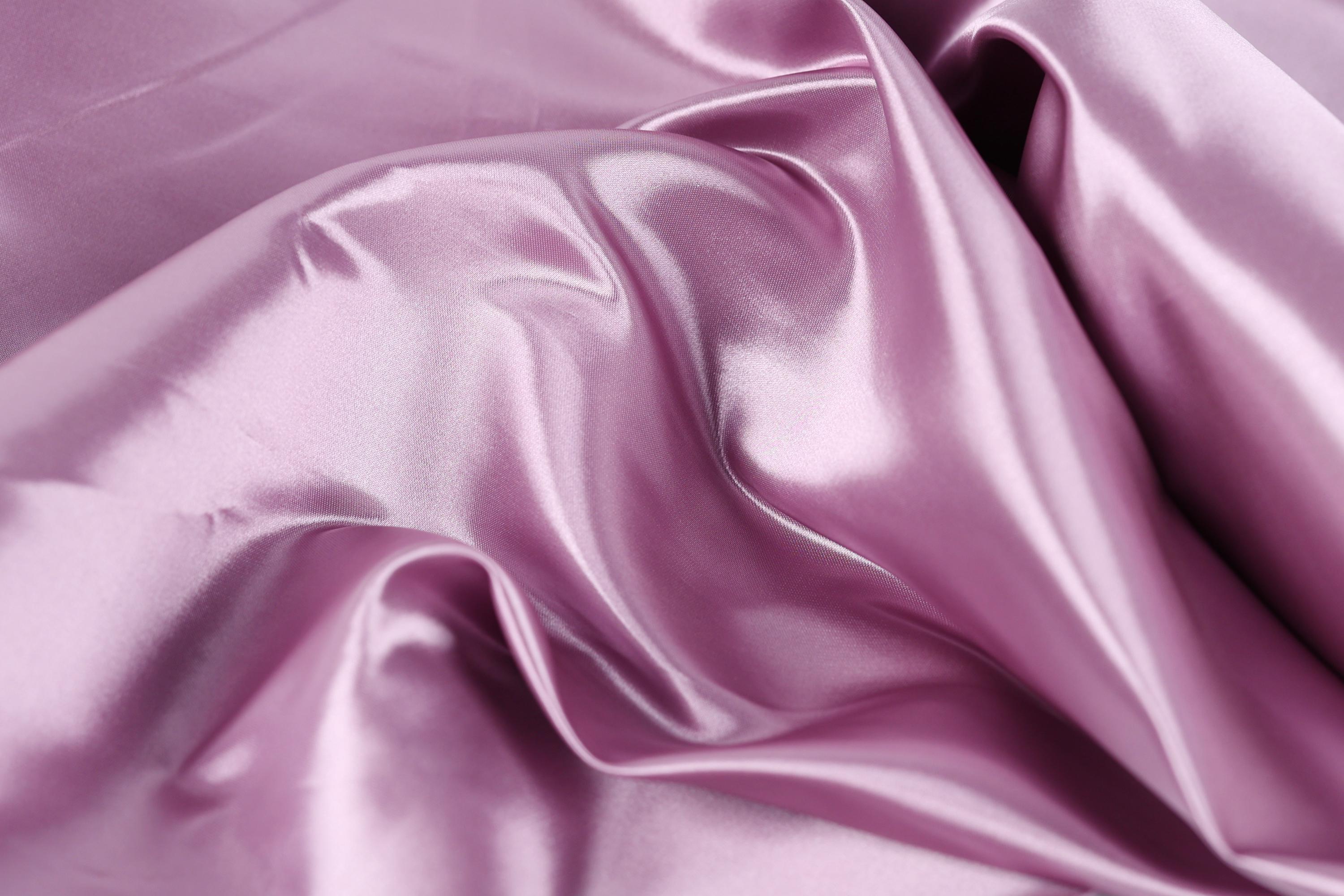 a close-up view of a soft, shiny, and smooth fabric in a deep purple color. The fabric appears to be made of satin or a similar material, with a smooth texture and a shiny appearance. The fabric is crumpled, giving it a slightly wrinkled and textured look.