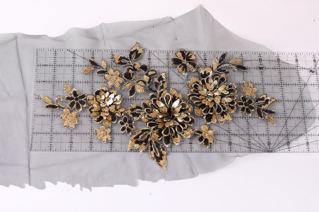 a close-up view of a piece of fabric with a floral pattern, including gold and black flowers, placed on a transparent ruler.