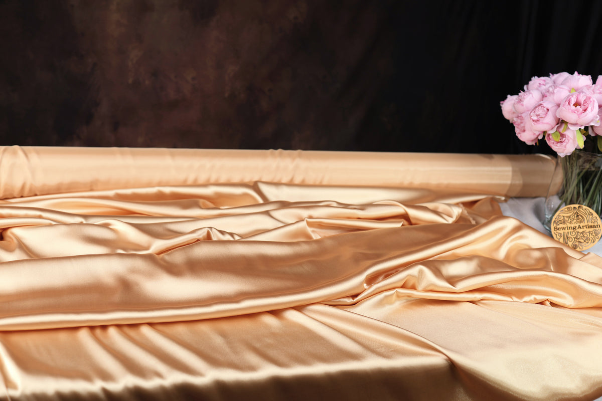 a luxurious gold fabric draped over a surface, with a vase of pink flowers placed next to it.