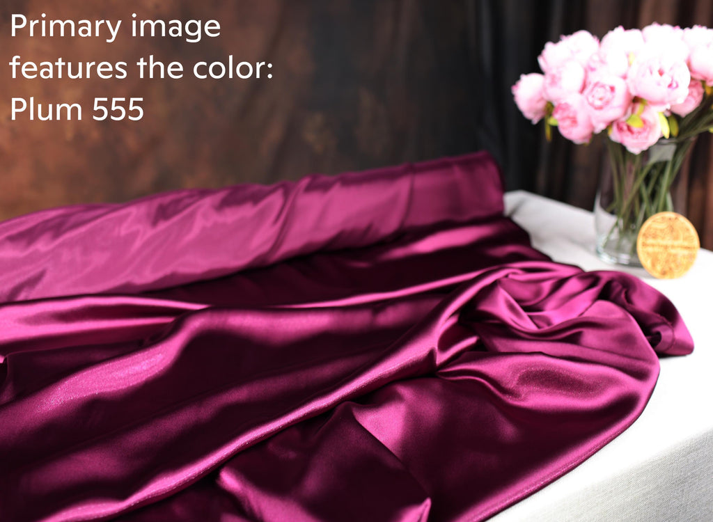 a close-up view of a piece of purple satin fabric, with a vase of pink flowers placed on a table next to it.