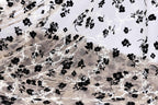 a close-up view of a fabric with a black and white floral pattern. The fabric appears to be made of sheer material, with the black flowers and leaves contrasting against the white background. The pattern is intricate and detailed, with the flowers and leaves filling the entire visible area of the fabric.