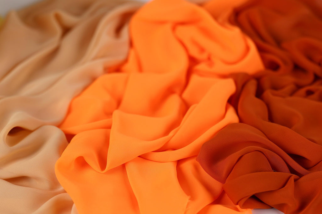 a close-up view of a pile of fabric, with a mix of orange and beige colors. The fabric appears to be crumpled and wrinkled, giving it a textured and soft appearance.