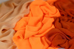 a close-up view of a pile of fabric, with a mix of orange and beige colors. The fabric appears to be crumpled and wrinkled, giving it a textured and soft appearance.