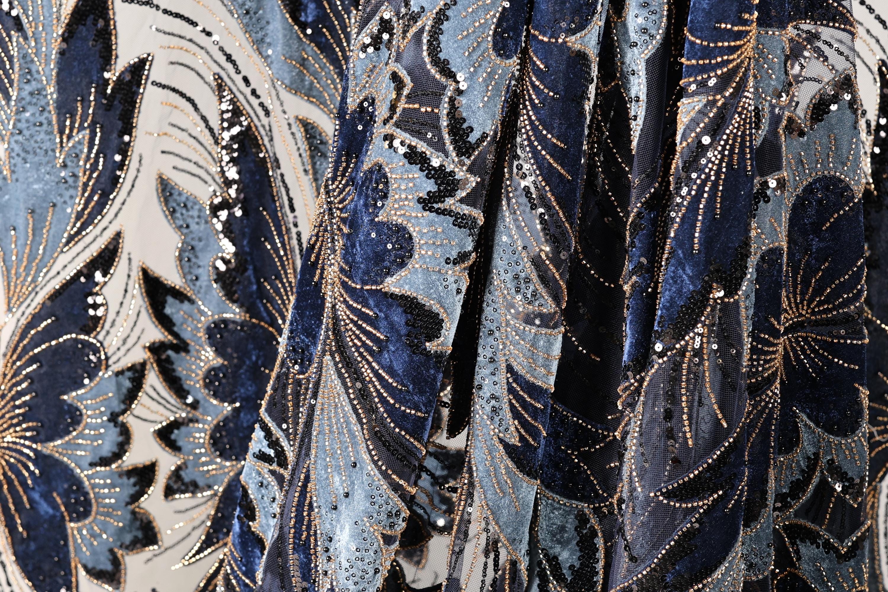 The image is a close-up of a fabric with a floral pattern, featuring blue and black colors and gold accents.