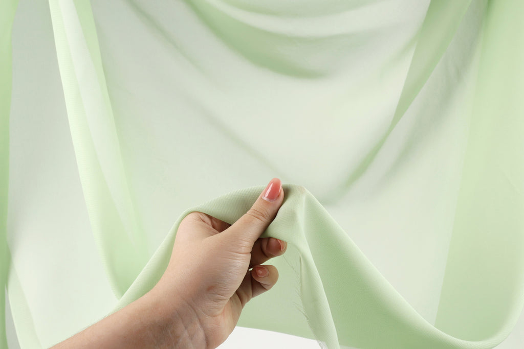A hand holding a piece of green fabric against a white background.
