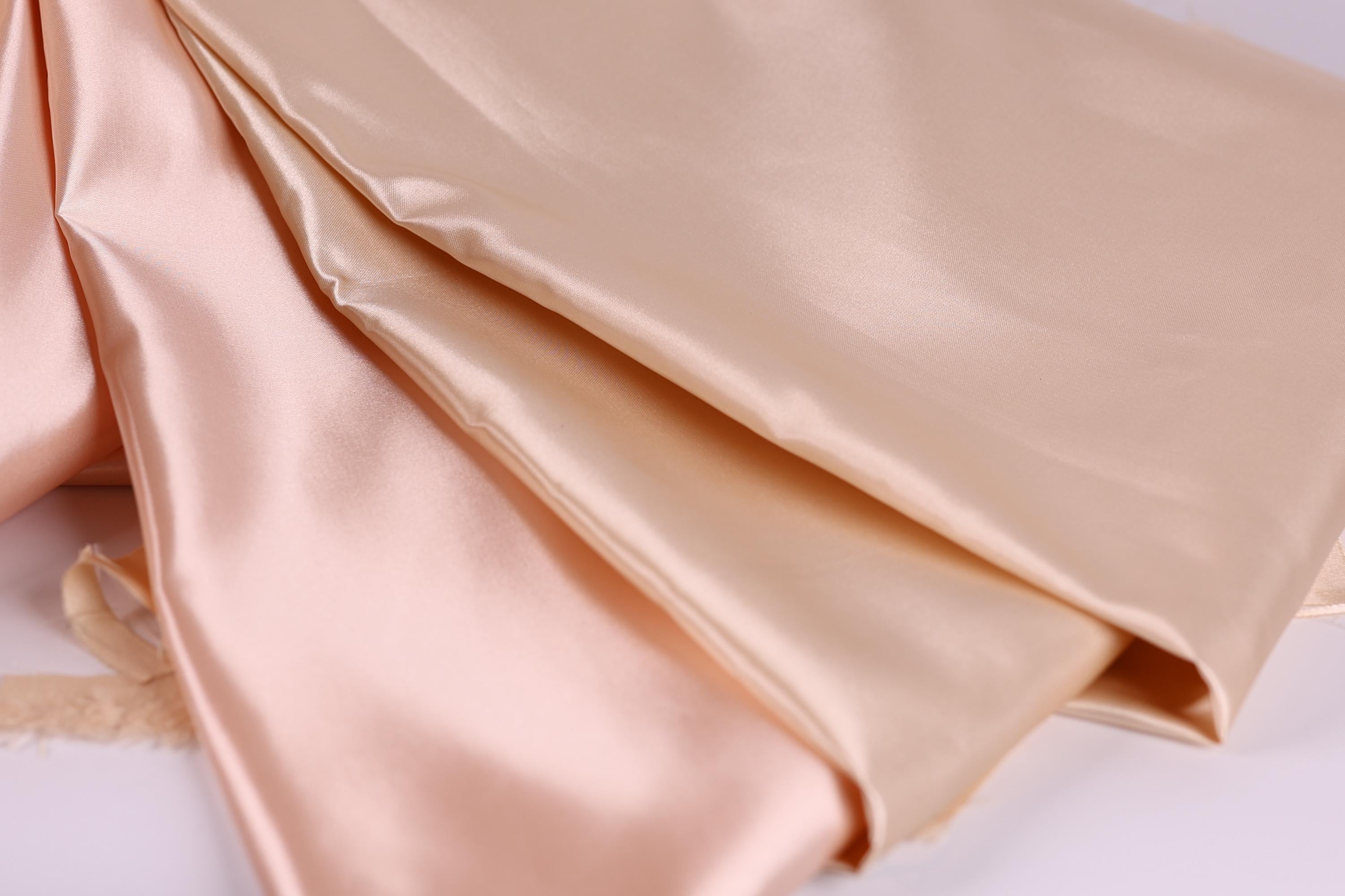 a close-up view of a soft, light-colored fabric, possibly silk or satin, with a smooth and shiny texture.