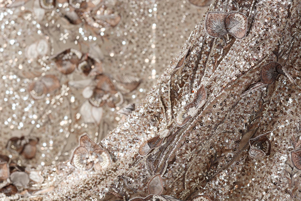 The image is a close-up of a fabric with a floral pattern, featuring a mix of brown and silver sequins and flowers.
