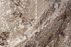 The image is a close-up of a fabric with a floral pattern, featuring a mix of brown and silver sequins and flowers.