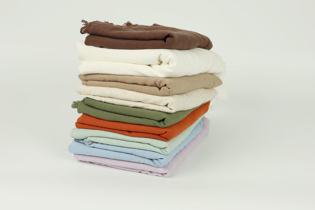A stack of various colored towels or cloths, including white, brown, green, orange, and blue, arranged in a visually appealing manner.