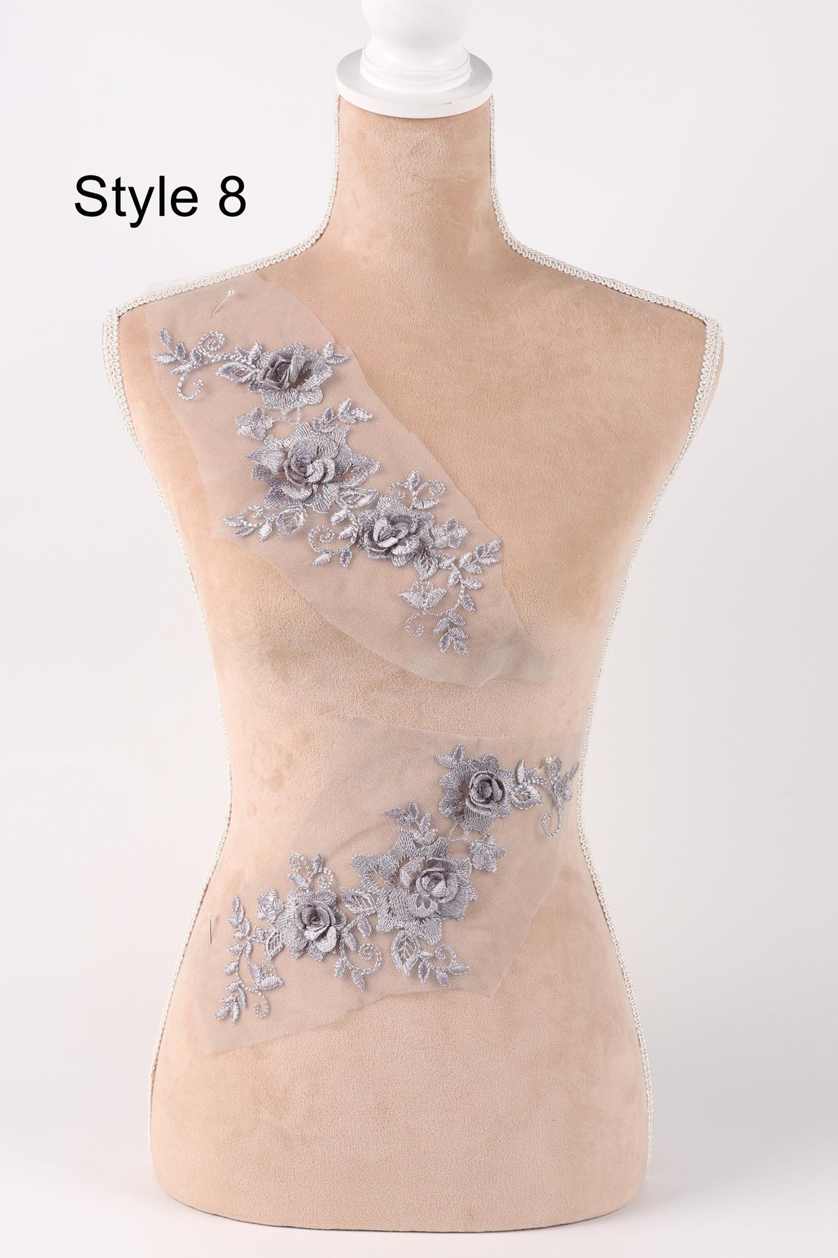 A mannequin with a beige body and a white head, wearing a dress with silver floral embroidery.