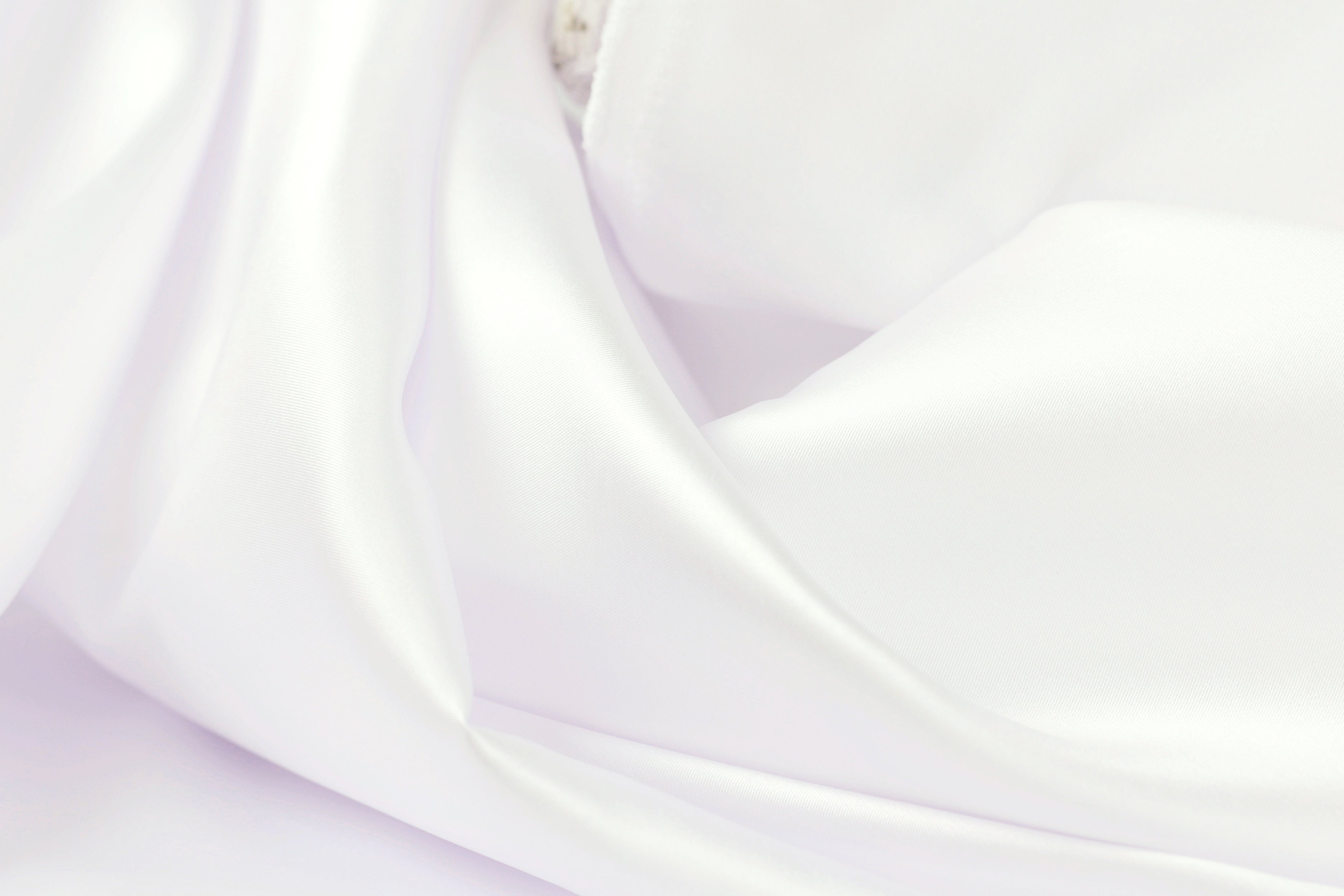 The image is a close-up of a soft, white fabric, possibly silk or satin, with a smooth and flowing texture.