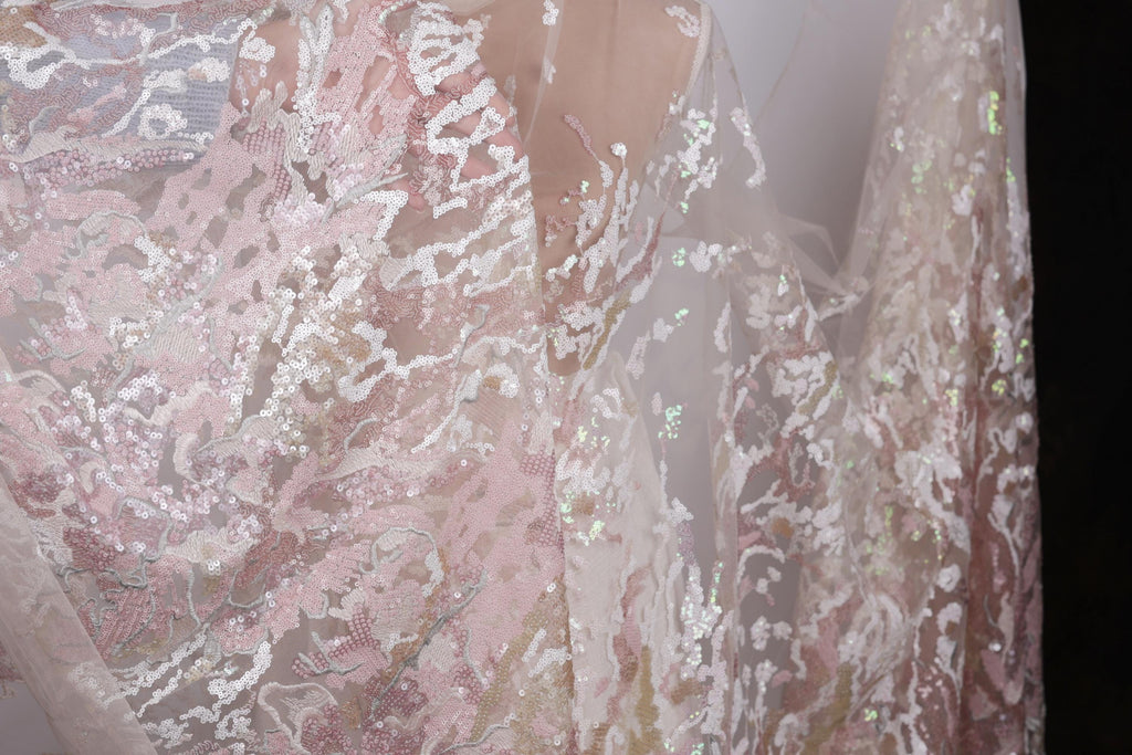 a close-up view of a delicate, lace-like fabric with a floral pattern in shades of pink and white. The fabric appears to be made of sheer material, giving it a delicate and airy appearance.