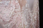 a close-up view of a delicate, lace-like fabric with a floral pattern in shades of pink and white. The fabric appears to be made of sheer material, giving it a delicate and airy appearance.