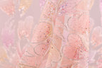 A close-up view of a delicate, pink fabric adorned with sparkling sequins and delicate floral patterns.
