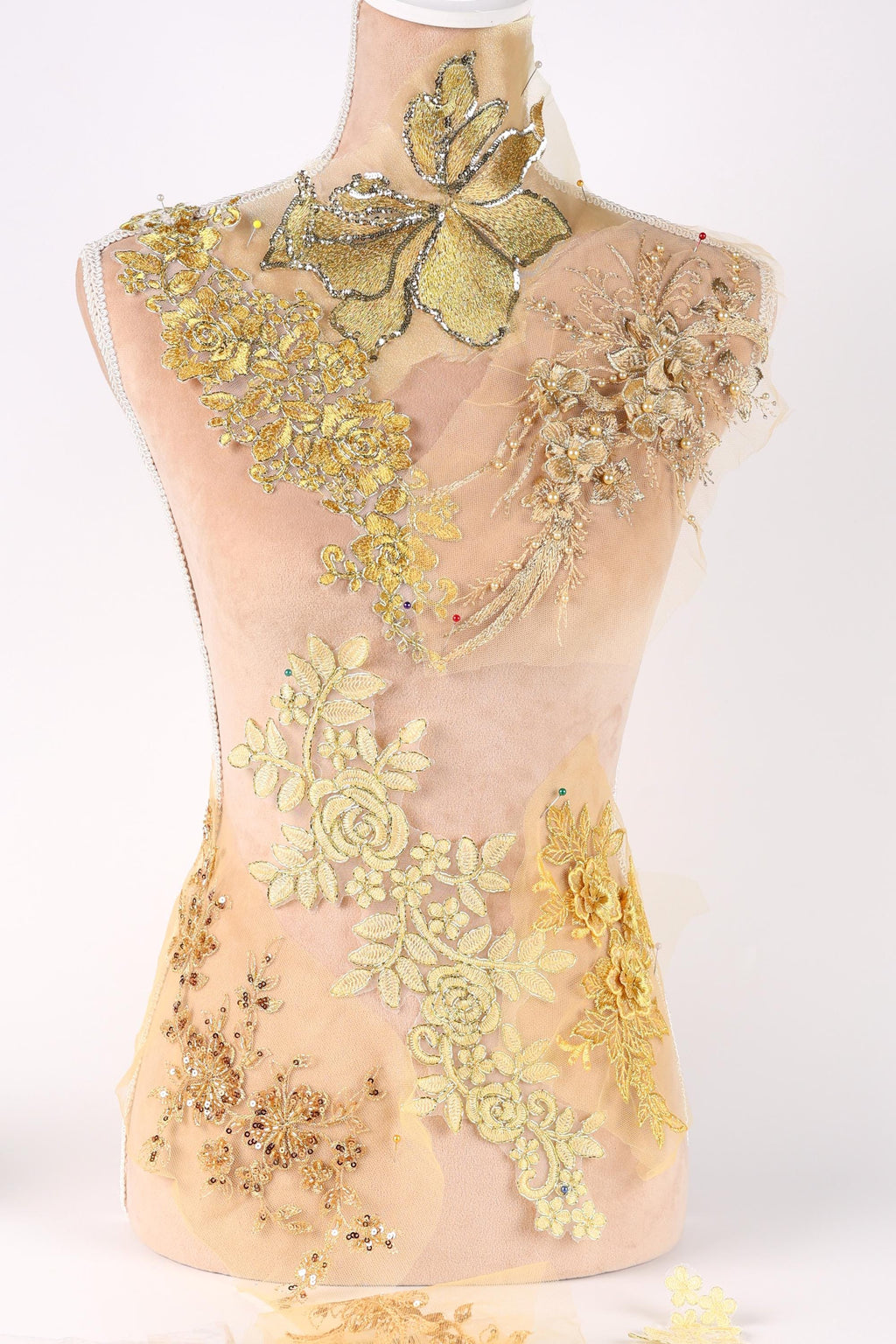 A mannequin wearing a dress with intricate gold and yellow embroidered designs, including flowers and leaves, covering the entire upper body.