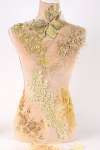 A mannequin wearing a dress with intricate gold and yellow embroidered designs, including flowers and leaves, covering the entire upper body.