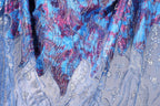 a close-up view of a fabric with a vibrant, multicolored pattern. The fabric appears to be a blend of blue, purple, and pink hues, with intricate designs and textures that create a visually striking and detailed appearance.