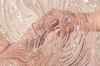 A close-up view of a hand holding a piece of pink and gold sequin fabric, with the fabric's intricate patterns and shimmering sequins visible.