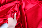 A hand is holding a piece of red satin fabric, with the fabric draped over the hand.