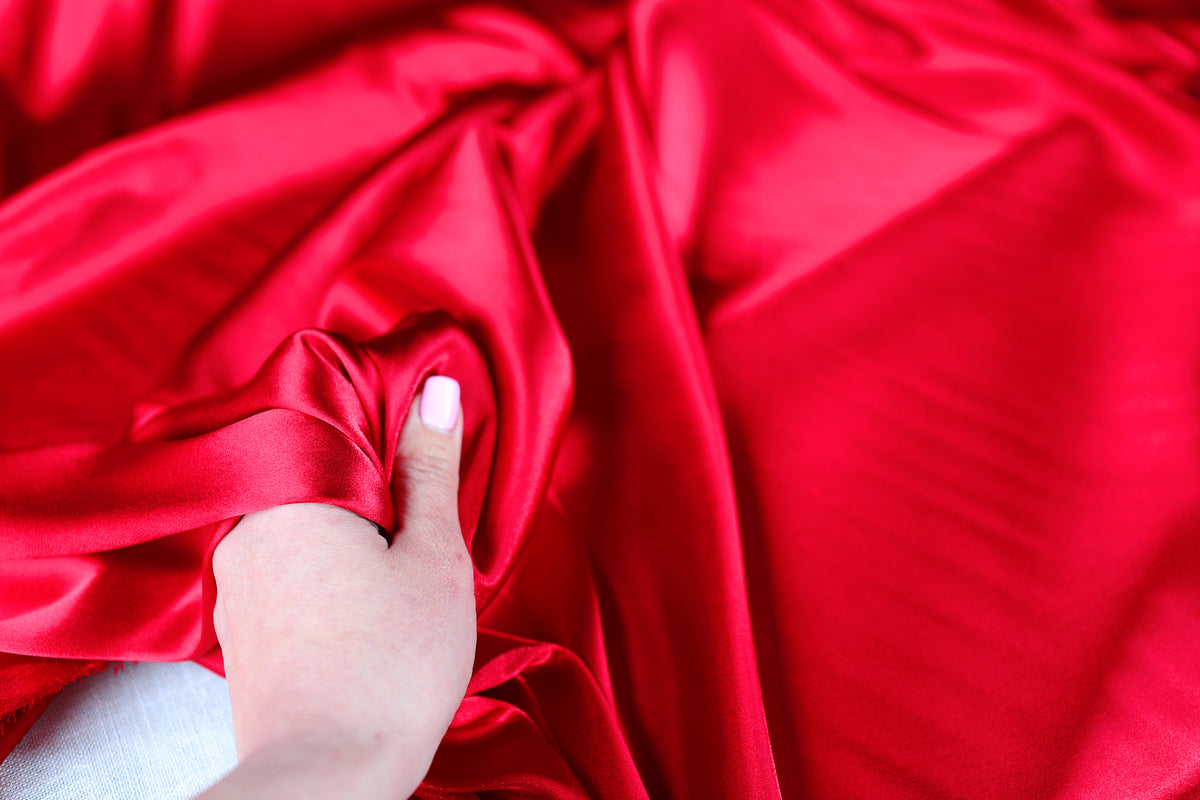 A hand is holding a piece of red satin fabric, with the fabric draped over the hand.