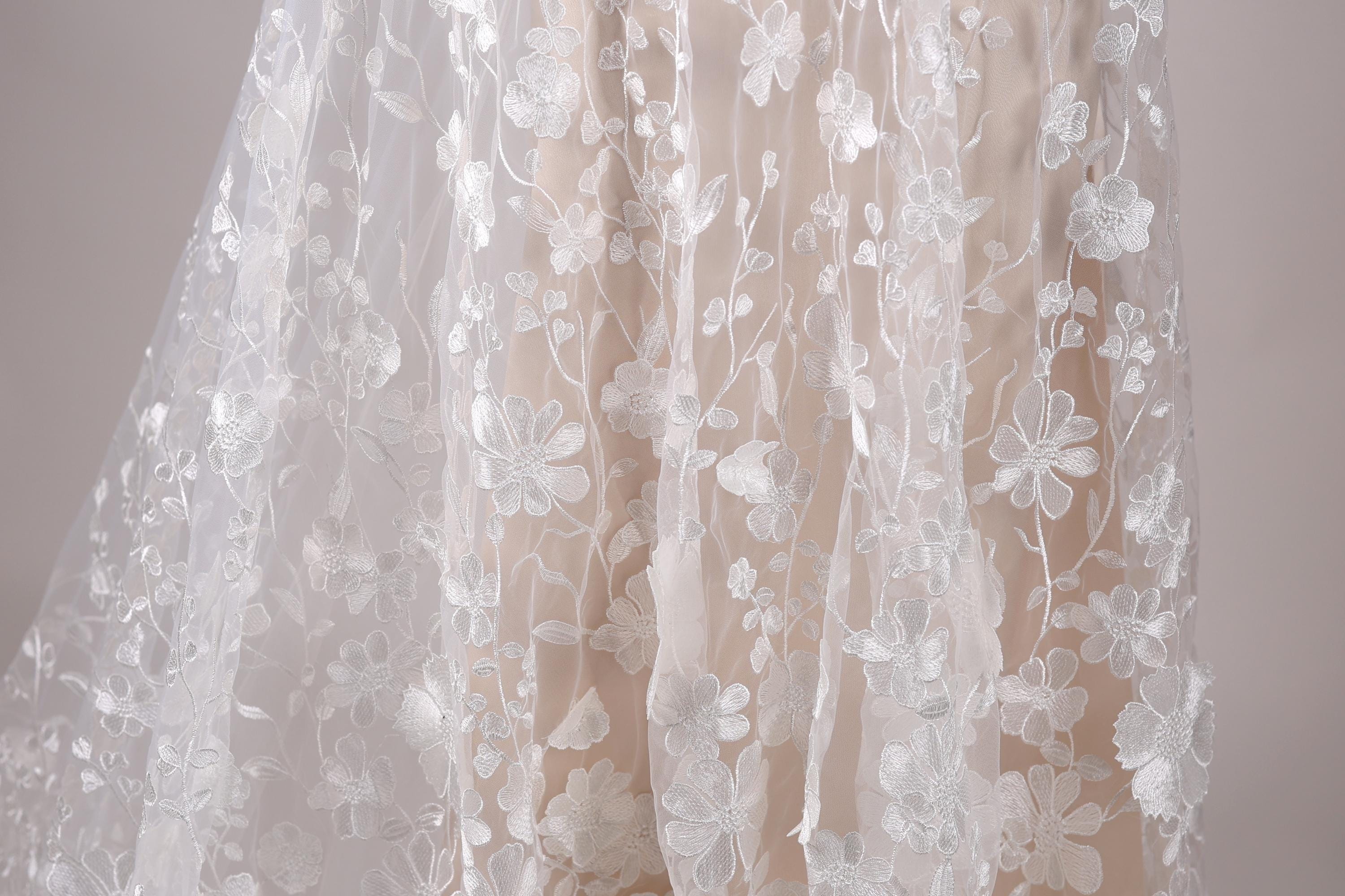 a close-up view of a delicate, white lace dress with a floral pattern.