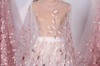 A mannequin wearing a white dress with pink floral embroidery on the skirt and a sheer, transparent fabric draped over the body.