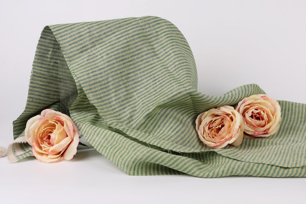 a green and white striped fabric with three delicate pink roses resting on it.