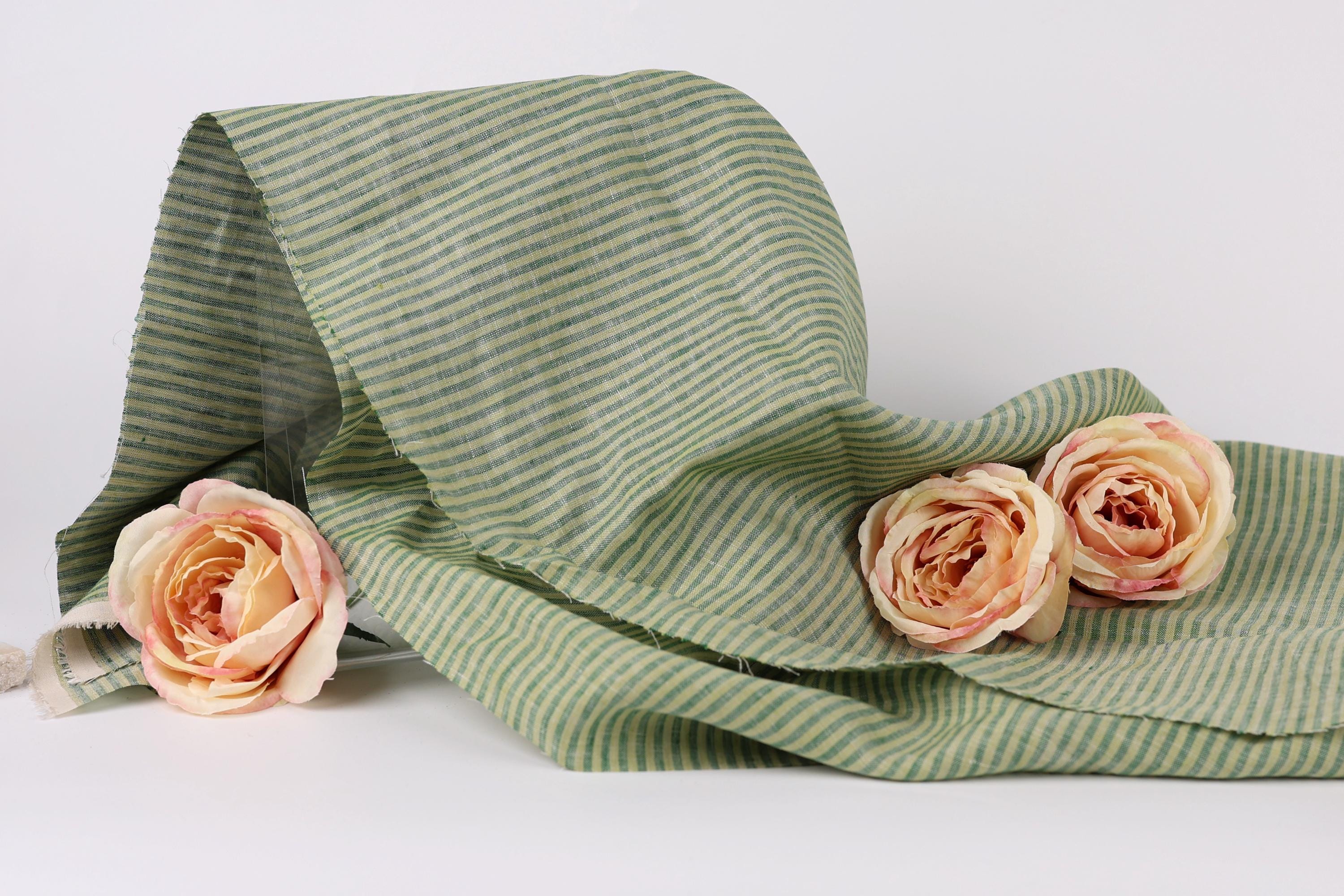 a green and white striped fabric with three delicate pink roses resting on it.