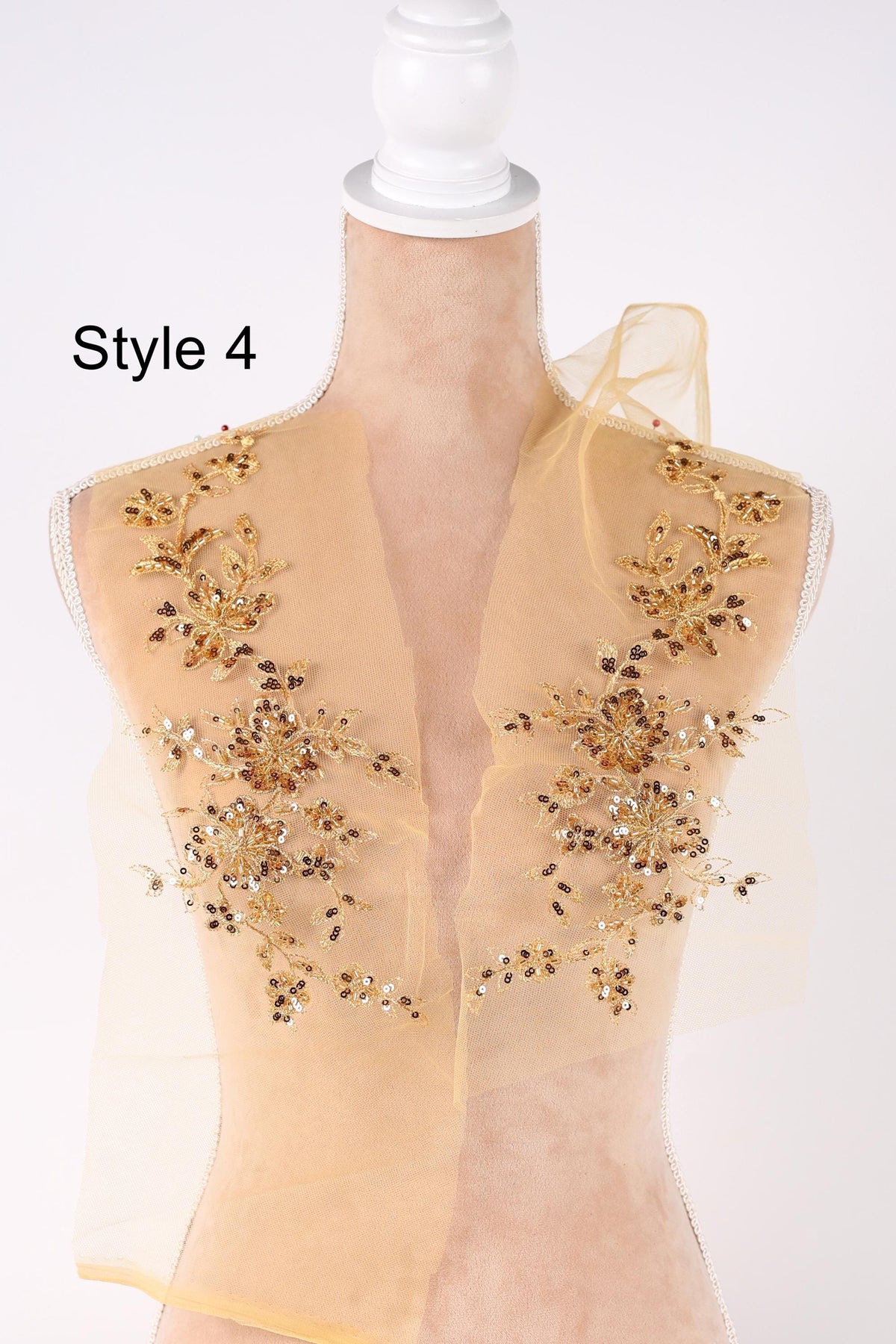 A mannequin with a beige dress and gold floral embellishments on the shoulders and back.