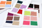 a collection of fabric swatches, each with a different color, arranged on white papers. The swatches are spread out, and some are overlapping, creating a collage-like effect.