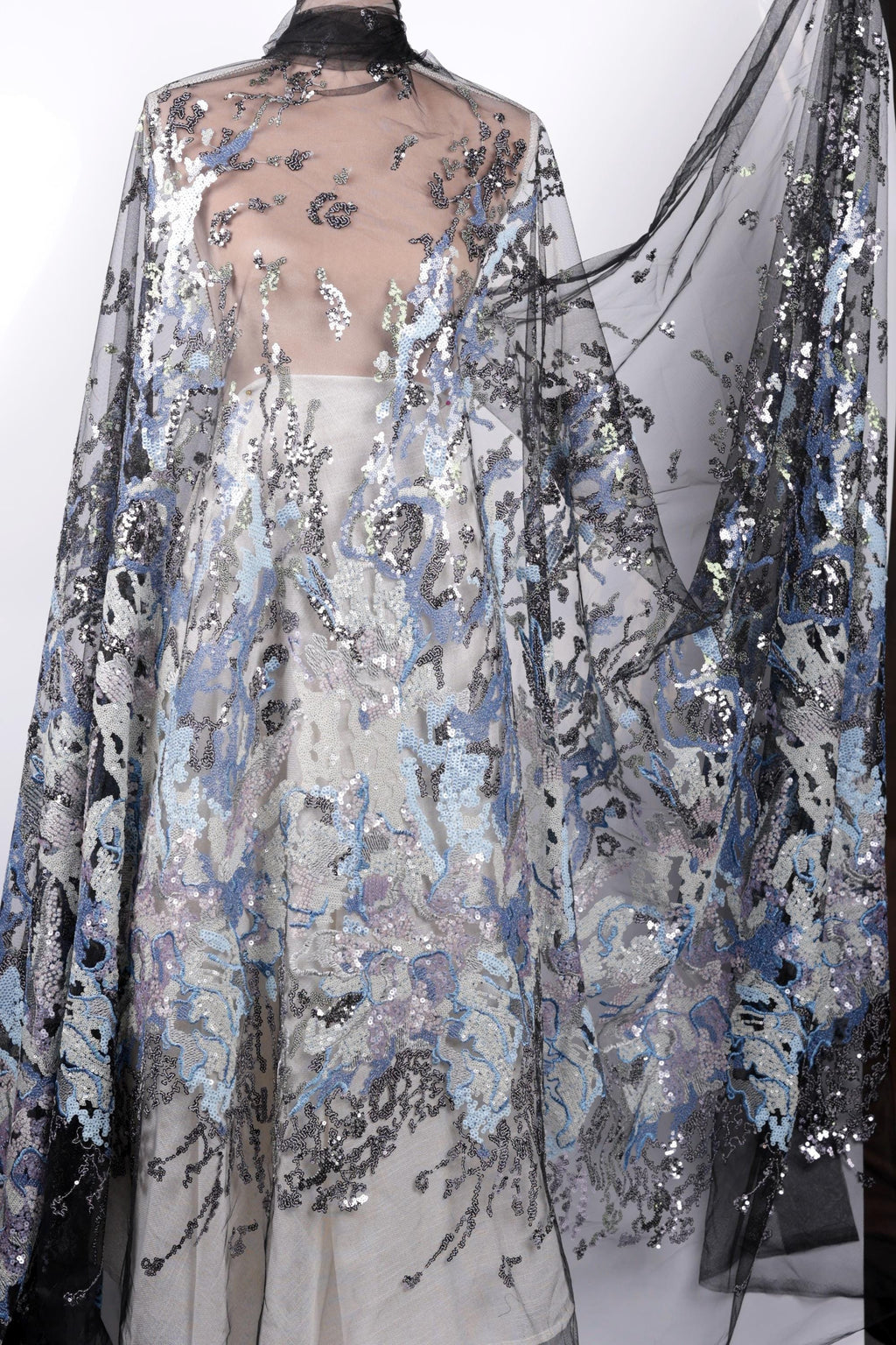 a long, flowing dress with a sheer, sheer-like fabric that has a floral pattern. The dress appears to be made of sequins or other embellishments, giving it a shiny and elegant appearance.