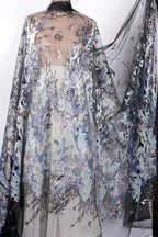 a long, flowing dress with a sheer, sheer-like fabric that has a floral pattern. The dress appears to be made of sequins or other embellishments, giving it a shiny and elegant appearance.