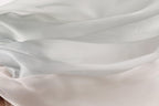 The image is a close-up of a soft, flowing fabric with a gradient of white and light gray colors. The fabric appears to be made of silk or a similar material, and it has a smooth, shiny texture. The colors are subtle, with the white and light gray shades blending together to create a soft, delicate appearance.