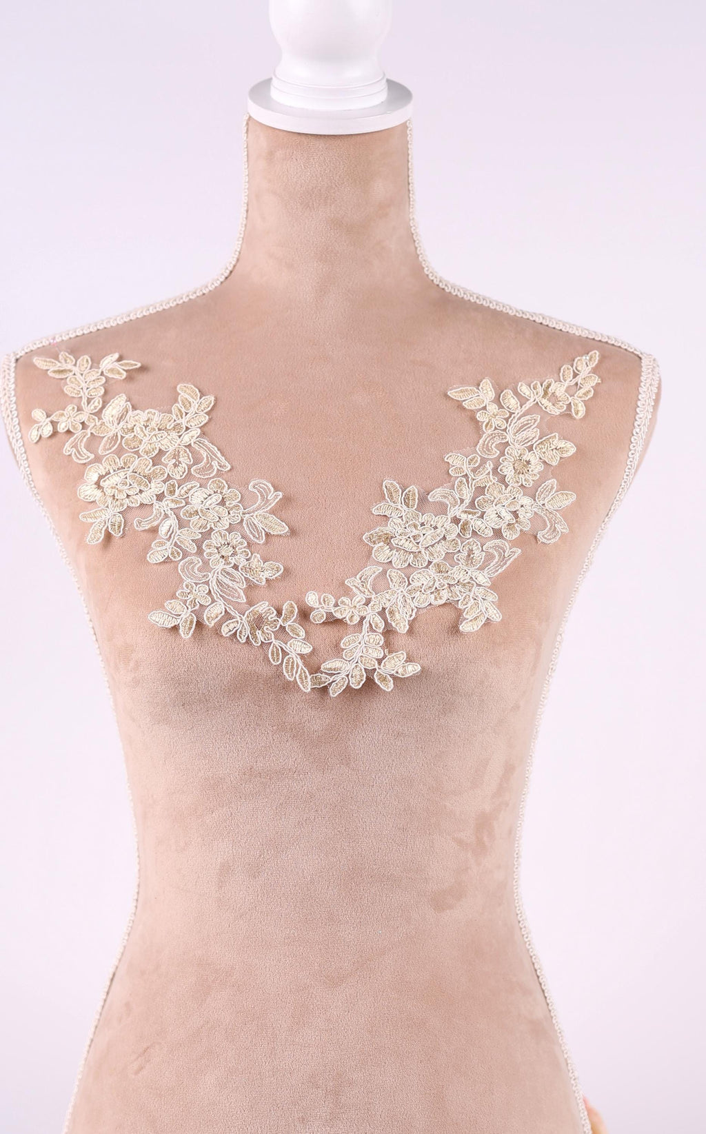 A mannequin wearing a beige dress with a delicate lace overlay on the neckline.