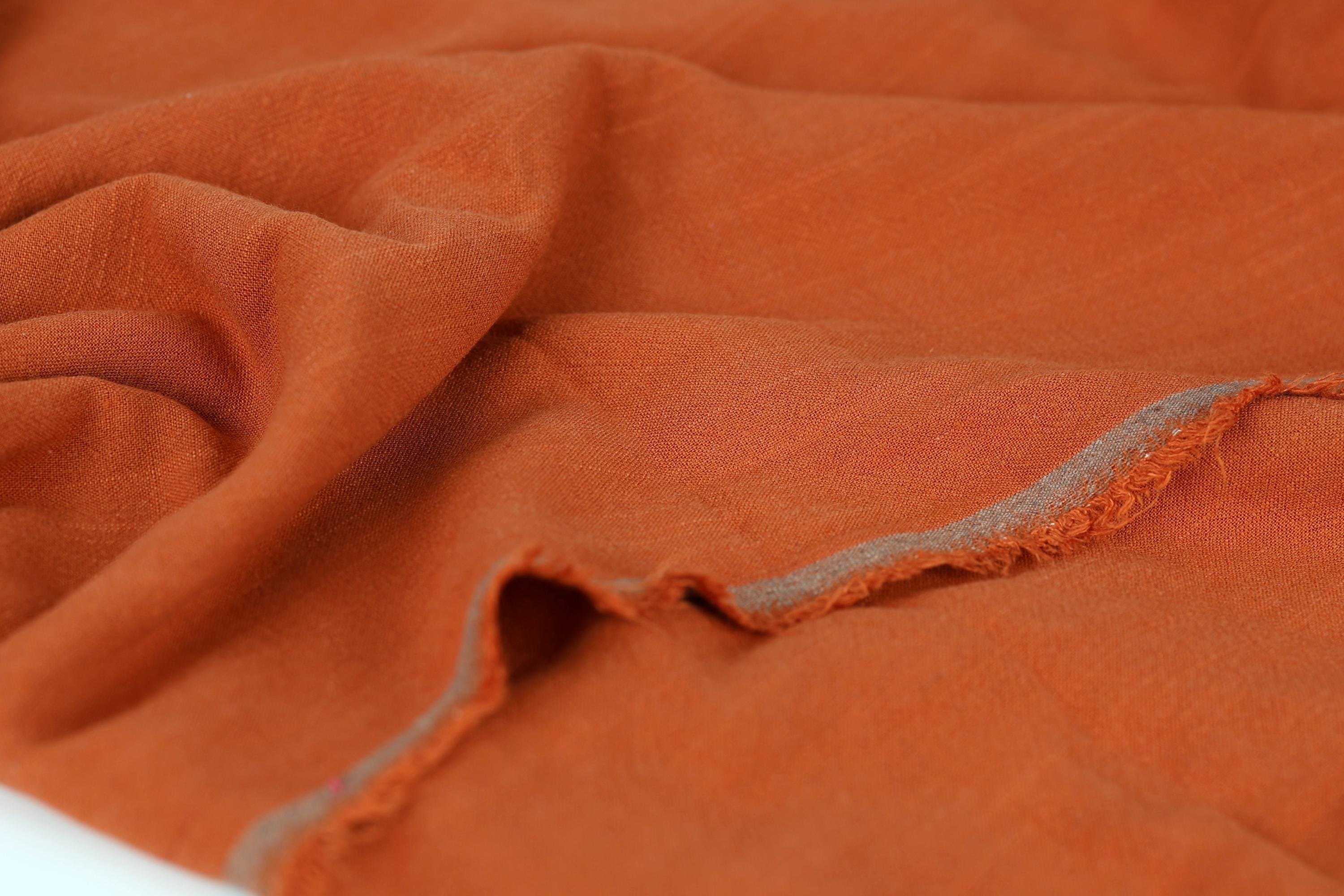 a close-up view of a crumpled orange fabric, with a small tear visible in the center.
