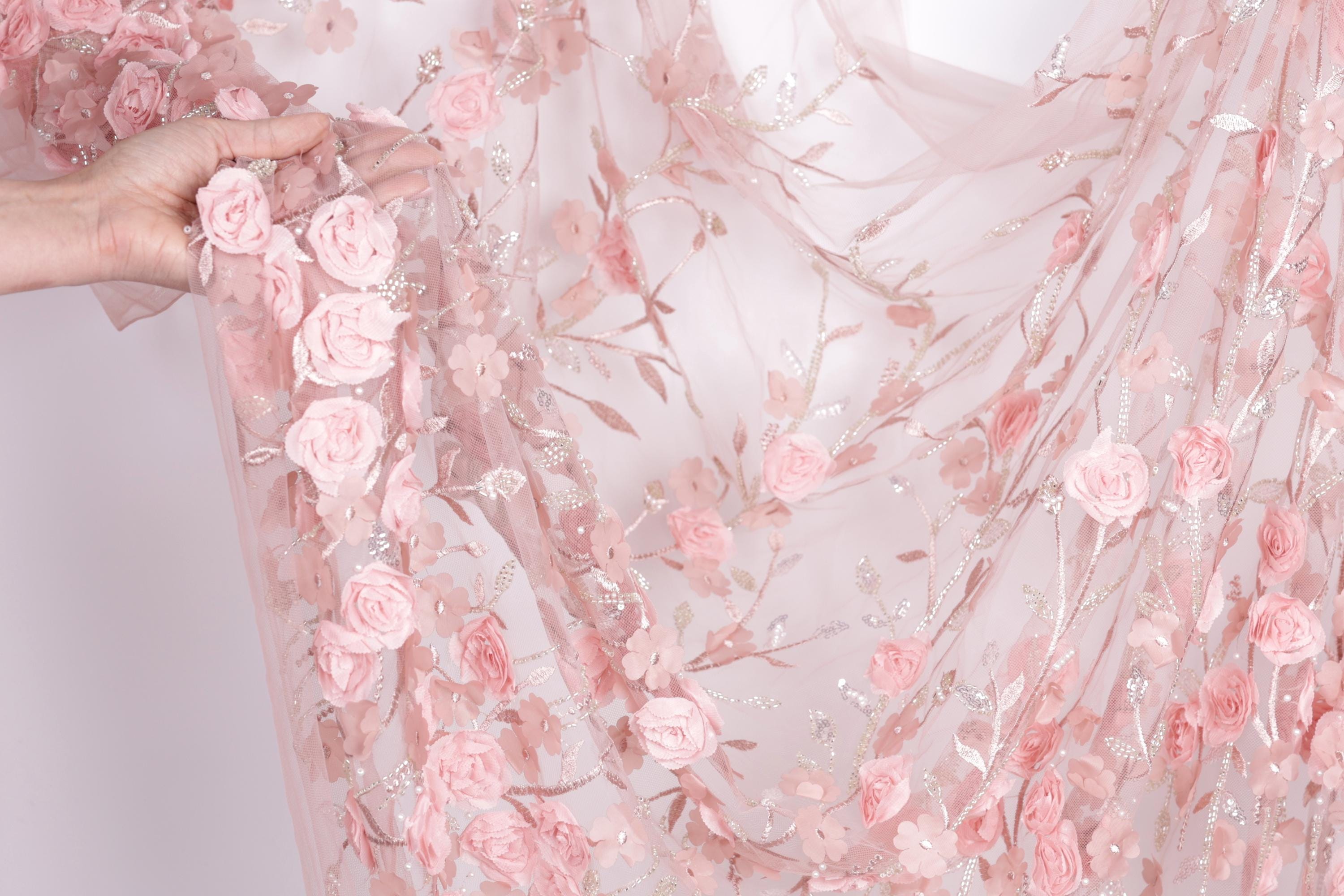A hand is holding a delicate piece of fabric adorned with a floral pattern of pink roses and leaves.