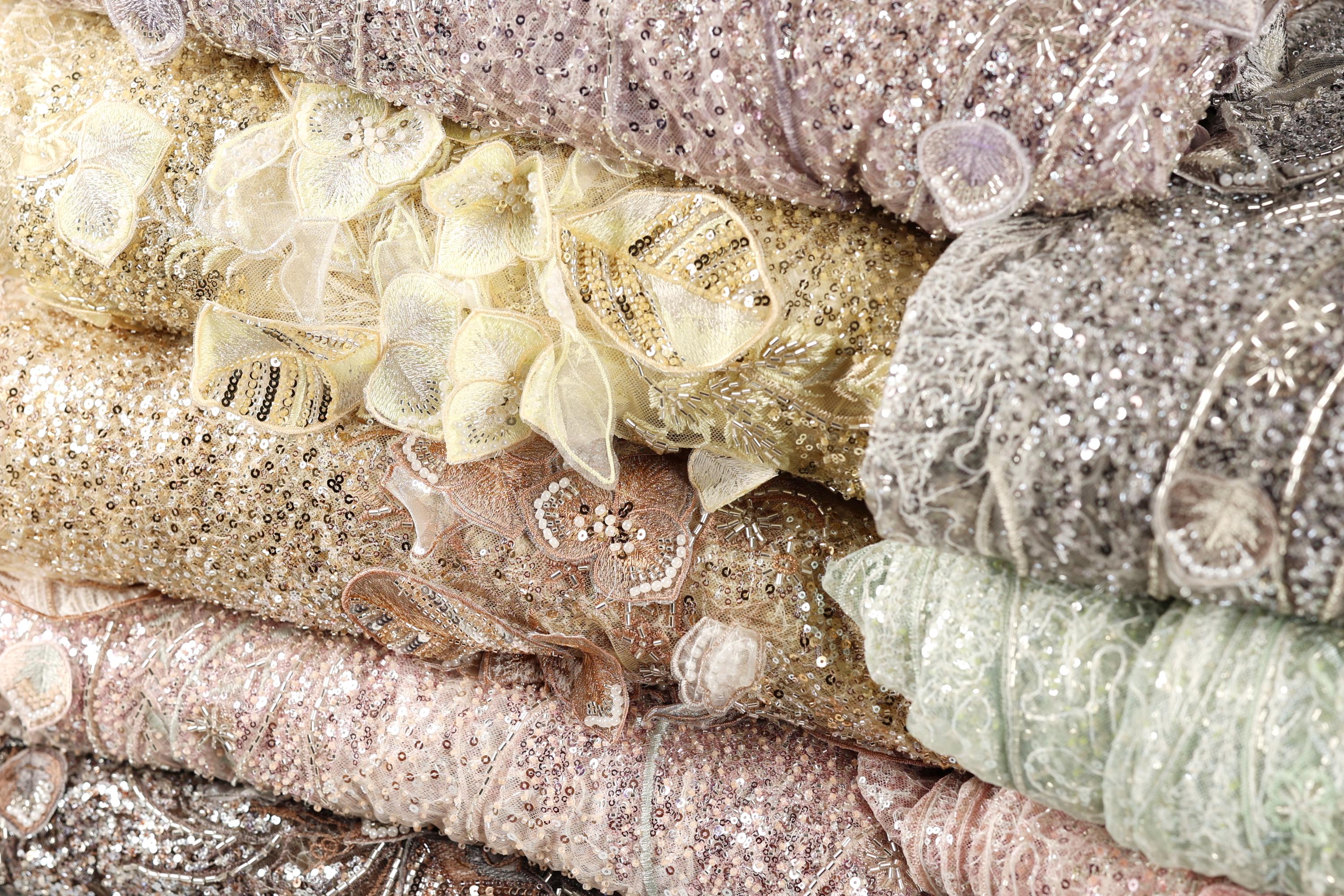 A close-up image of various colorful and intricately designed fabric pieces, including sequins and lace, stacked on top of each other.