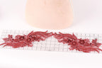 a decorative red lace piece with intricate floral patterns, placed on a ruler for scale.