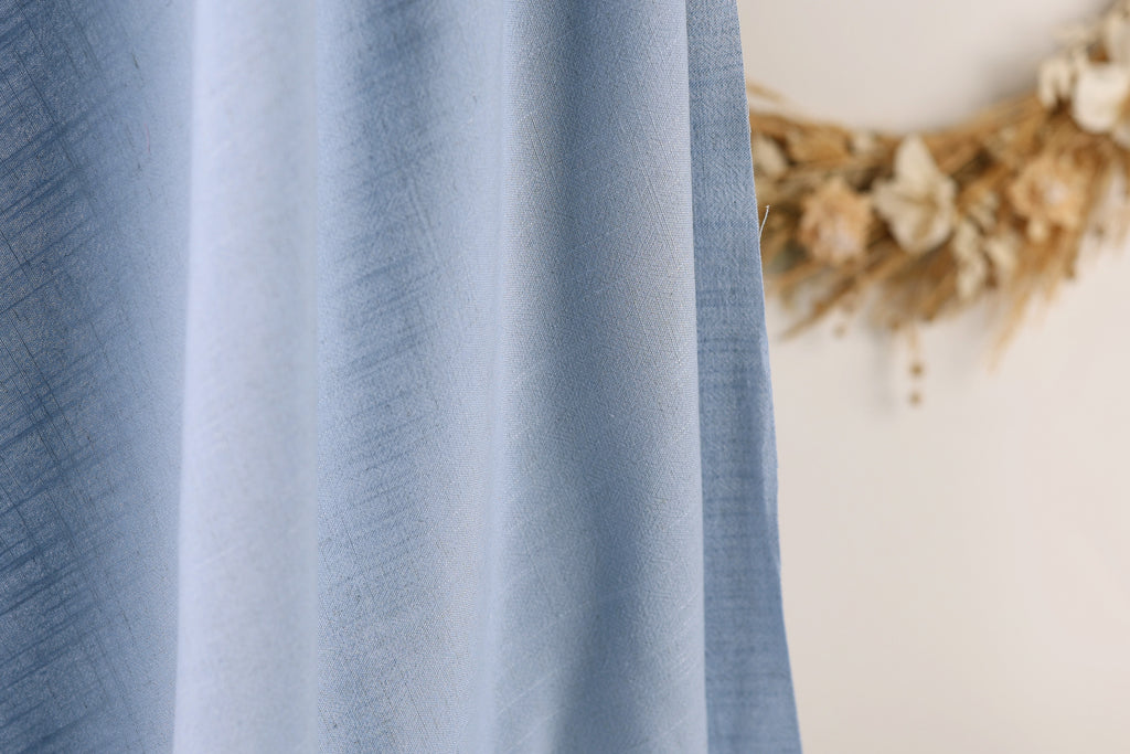 a close-up view of a blue fabric, with a blurred background featuring a wreath made of dried flowers.