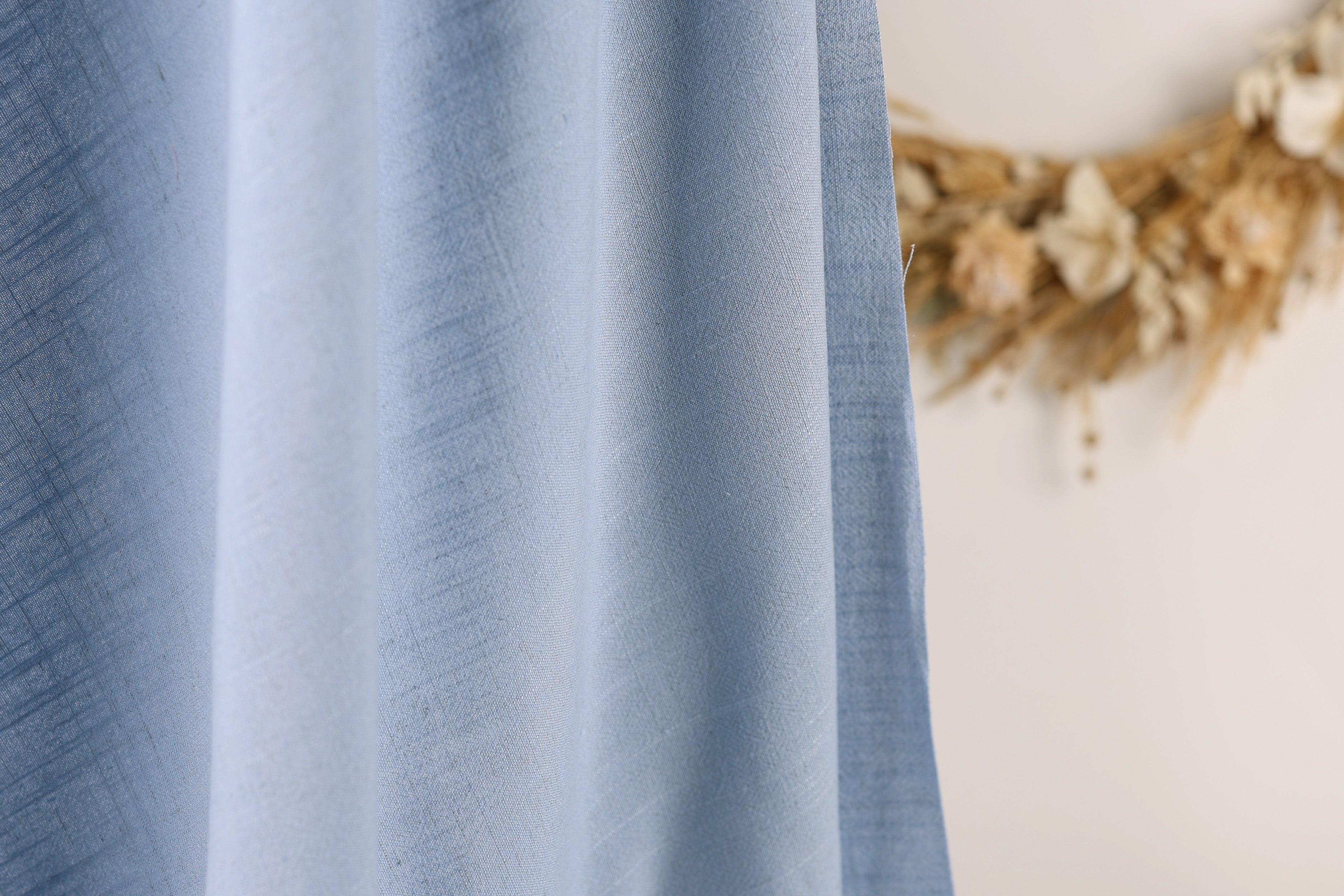 a close-up view of a blue fabric, with a blurred background featuring a wreath made of dried flowers.
