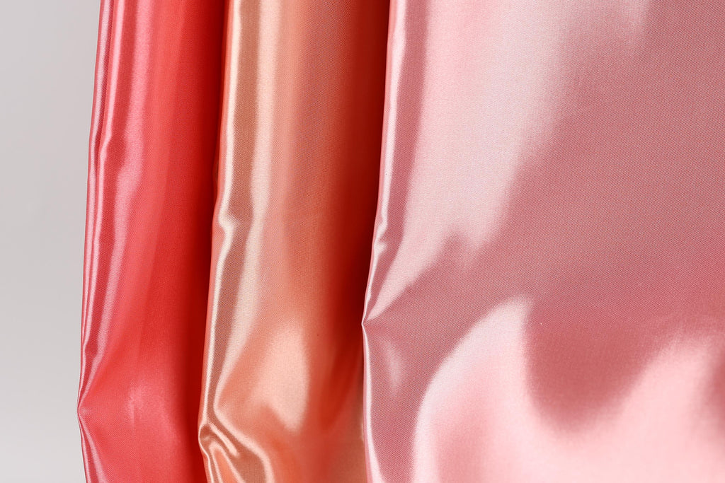 three different colored satin fabrics, with the colors being red, orange, and pink. The fabrics appear to be shiny and smooth, suggesting they are made of a shiny, satin-like material.