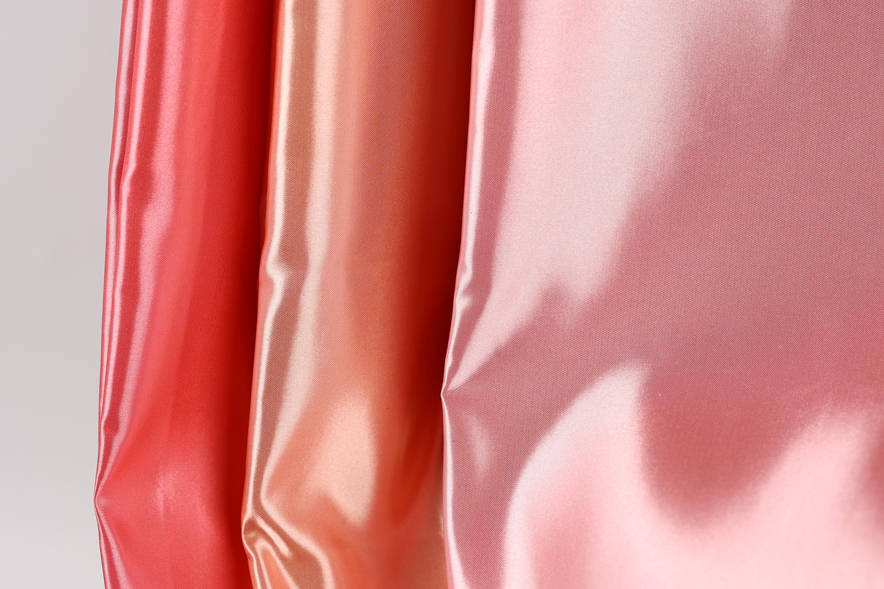three different colored satin fabrics, with the colors being red, orange, and pink. The fabrics appear to be shiny and smooth, suggesting they are made of a shiny, satin-like material.