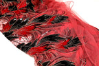 a close-up view of a fabric with a striking red and black floral pattern. The fabric appears to be made of a sheer material, giving it a delicate and airy appearance. The pattern consists of various shapes and designs, including leaves, flowers, and other decorative elements, all rendered in bold red and black colors. The fabric is spread out on a white surface, allowing the viewer to appreciate the intricate details and textures of the design.