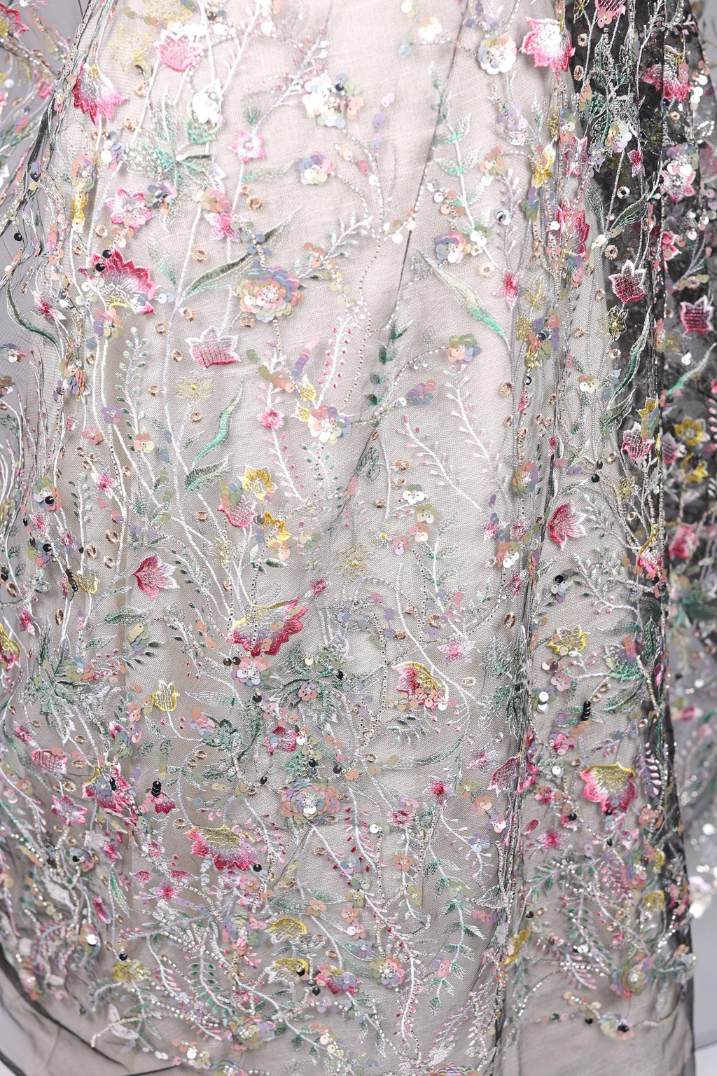 The image is a close-up of a delicate, intricately embroidered fabric with a floral pattern. The fabric is adorned with numerous small flowers and leaves, creating a visually appealing and detailed design. The image does not contain any text or other discernible objects, and the focus is solely on the intricate embroidery work.