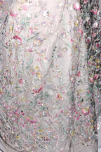 The image is a close-up of a delicate, intricately embroidered fabric with a floral pattern. The fabric is adorned with numerous small flowers and leaves, creating a visually appealing and detailed design. The image does not contain any text or other discernible objects, and the focus is solely on the intricate embroidery work.