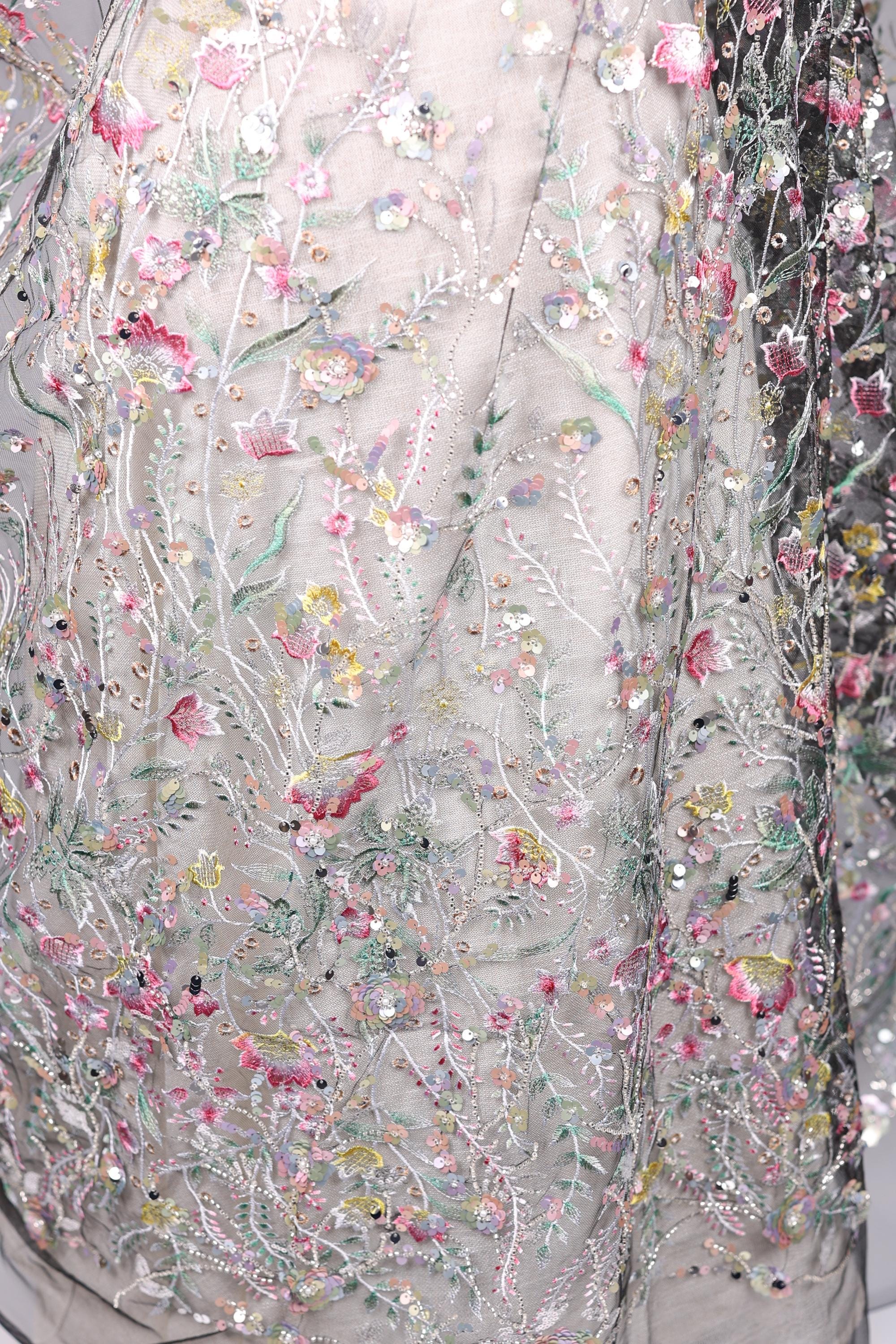 The image is a close-up of a delicate, intricately embroidered fabric with a floral pattern. The fabric is adorned with numerous small flowers and leaves, creating a visually appealing and detailed design. The image does not contain any text or other discernible objects, and the focus is solely on the intricate embroidery work.